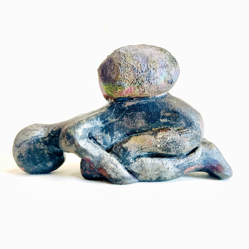 A clay sculpture of a human-like character supporting a stone on their knees, with several different shades and tones across the surface.